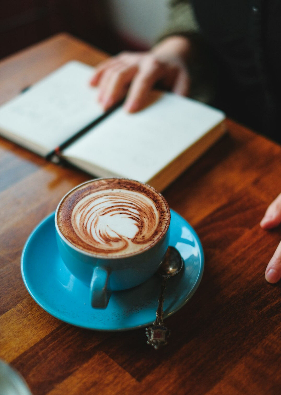 Person writing in a journal next to a cup of coffee